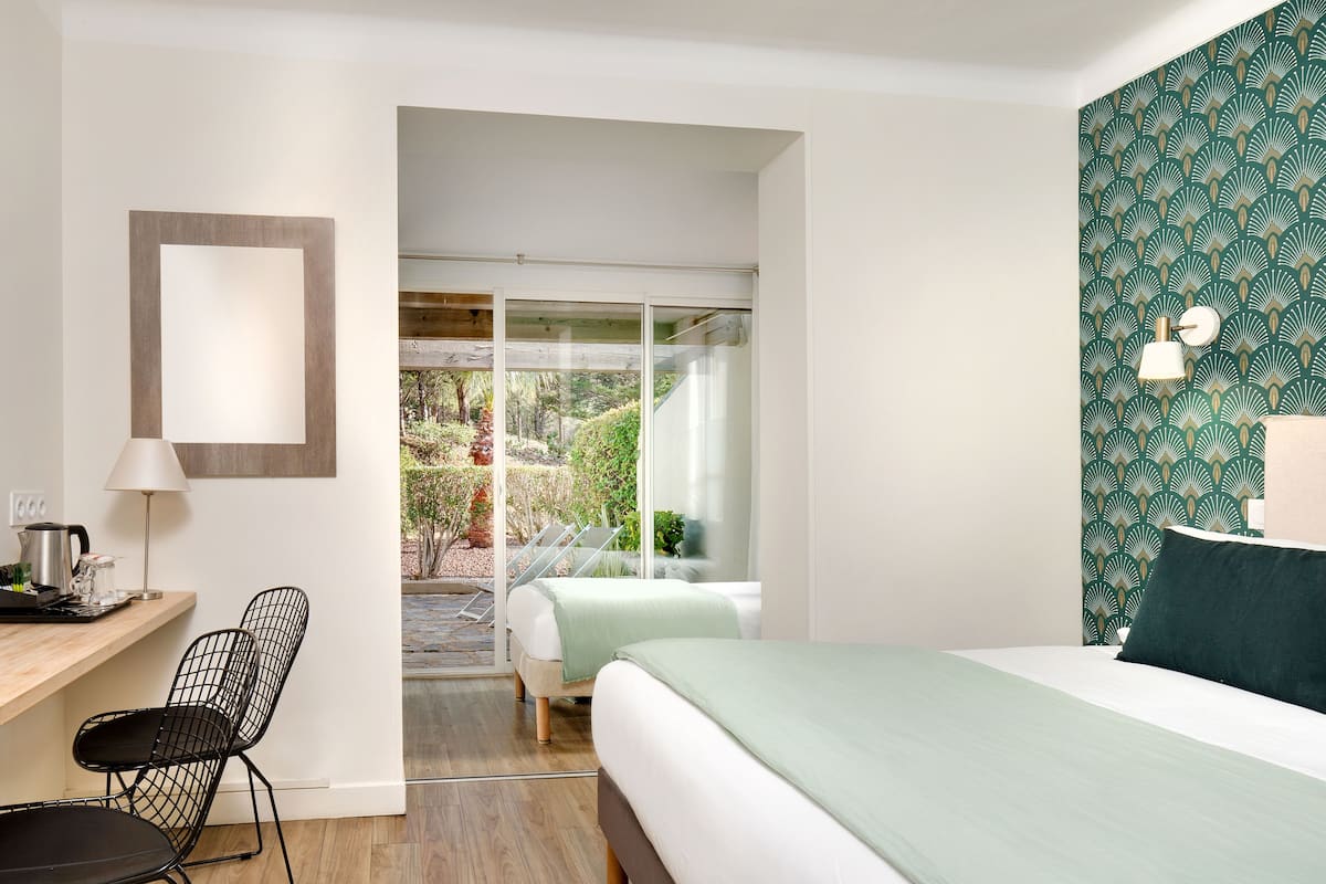 A modern hotel room with a bed, a desk, a chair, and a view of a garden through a glass door.