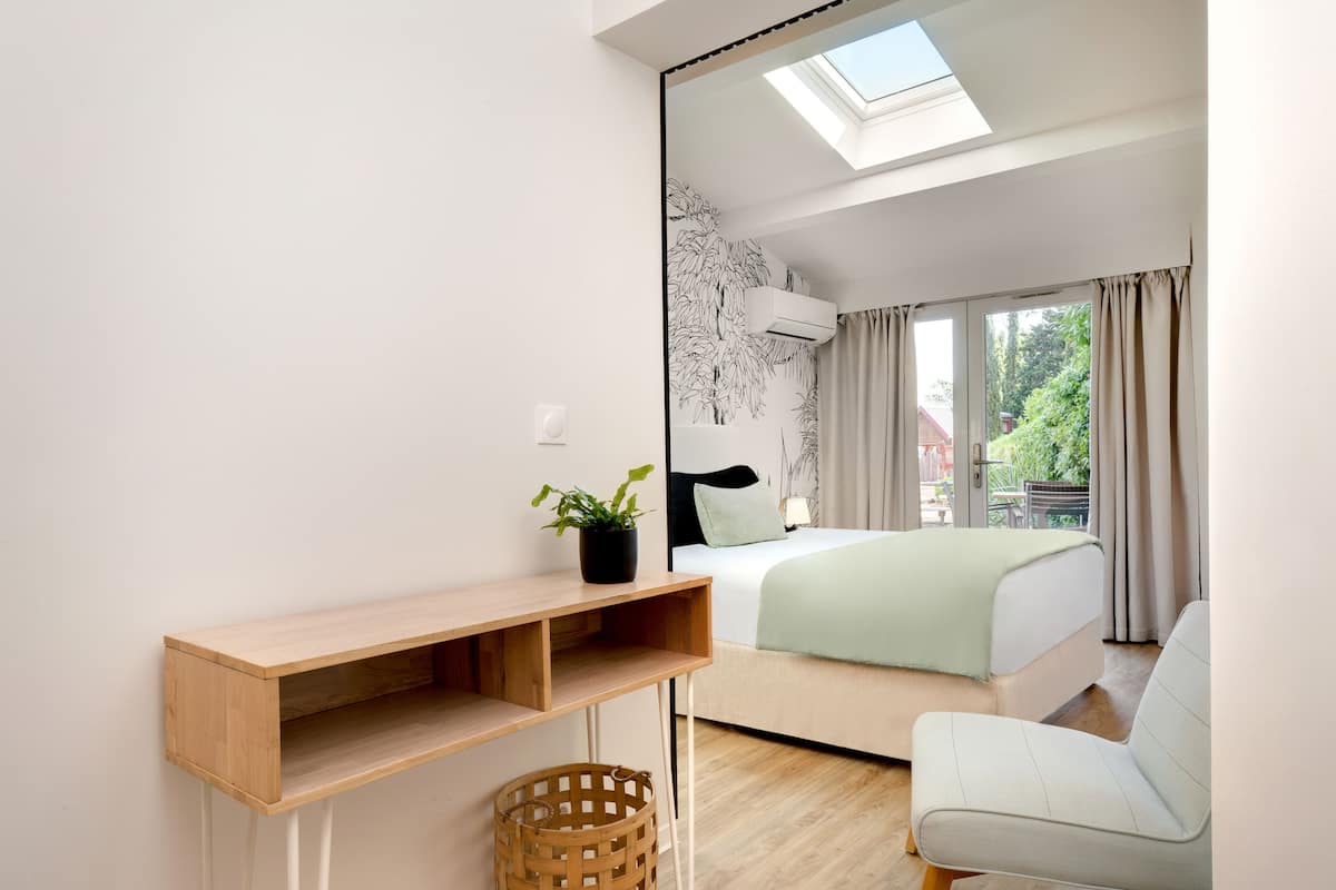 A modern bedroom with a skylight, a bed with a green blanket, a white chair, and a wooden desk.