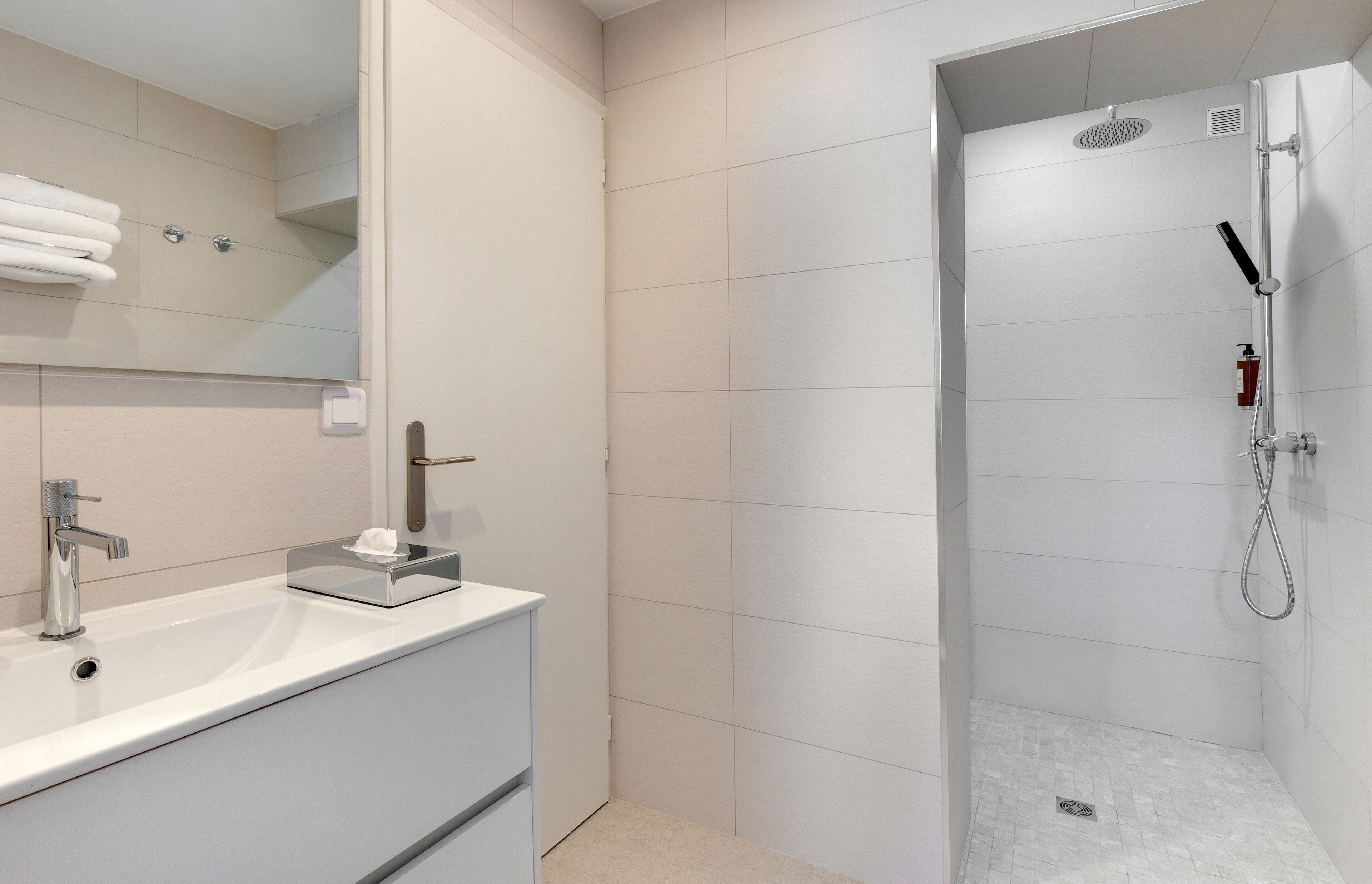 A modern bathroom with a white sink, mirror, and shower.