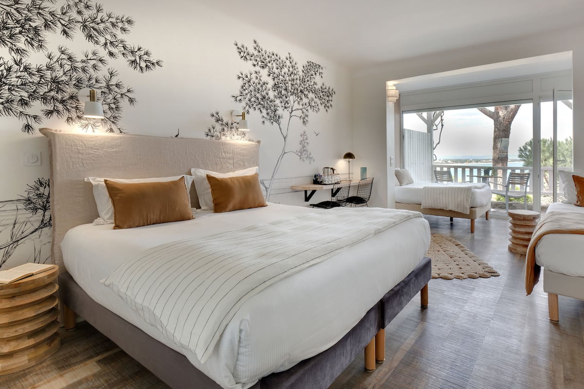 A modern bedroom with a large bed, a desk, and a view of the ocean.