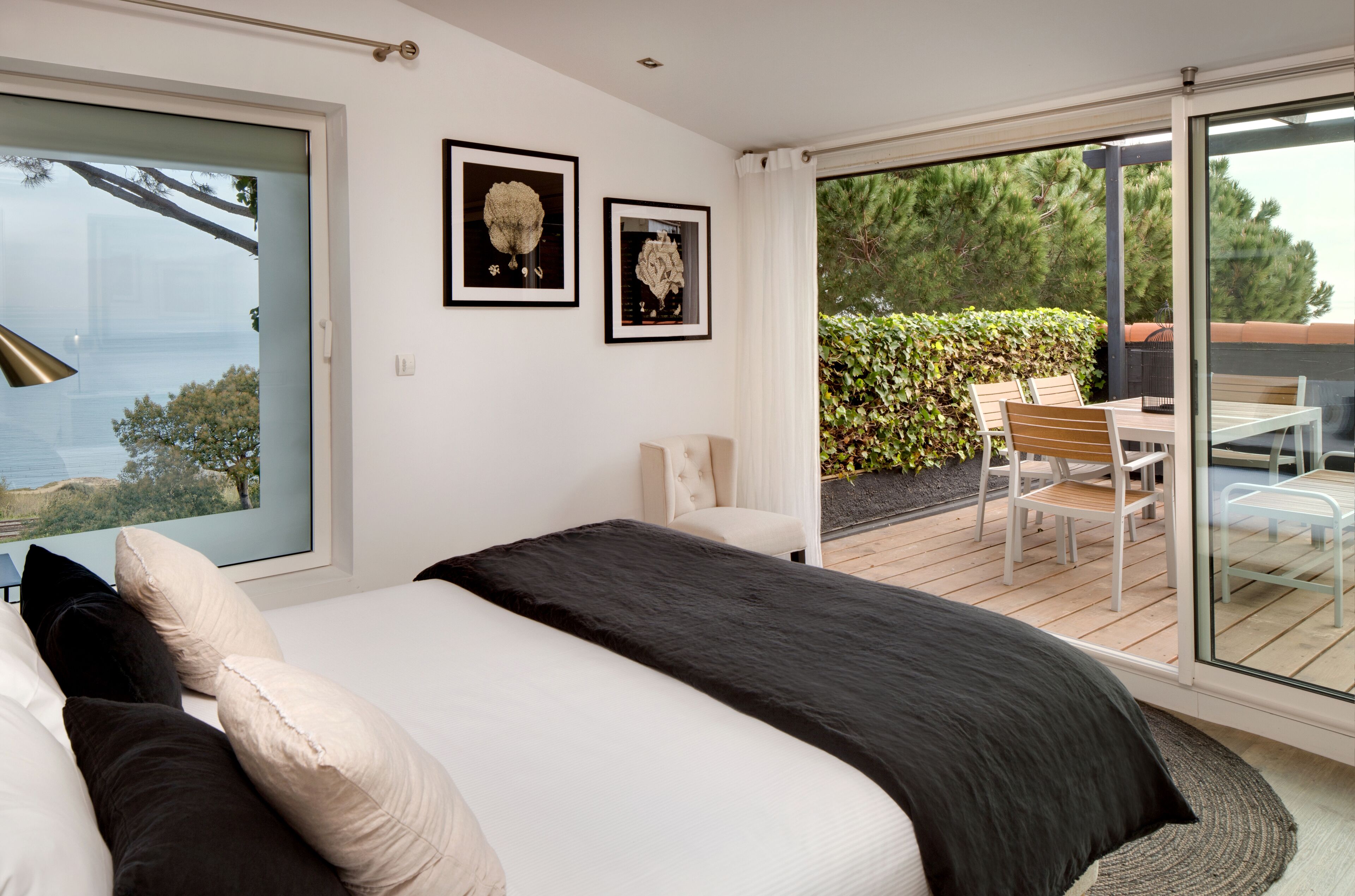 Un dormitorio con una cama grande, un ventanal corredero a un balcón y dos cuadros en la pared.