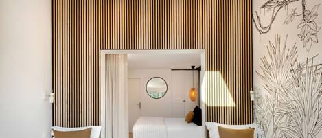 Una habitación de hotel moderna con una cama, dos mesitas de noche, una pequeña mesa de centro y un ventanal grande.