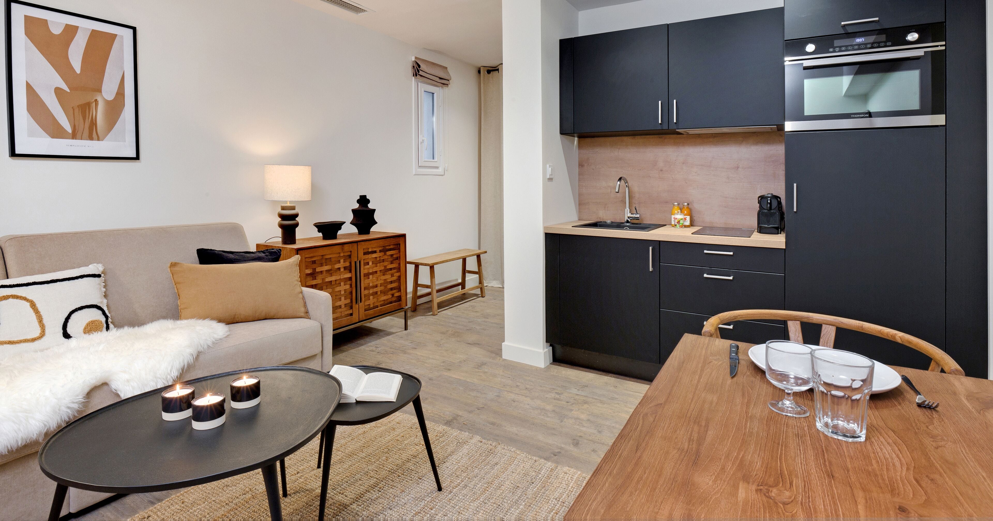 Una sala de estar moderna con un sofá, una mesa de centro con velas y un comedor con una mesa de madera y sillas.