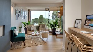 Una sala moderna con un sofá, sillas, una mesa de centro y plantas en macetas. Hay un escritorio con una computadora y vistas al exterior.