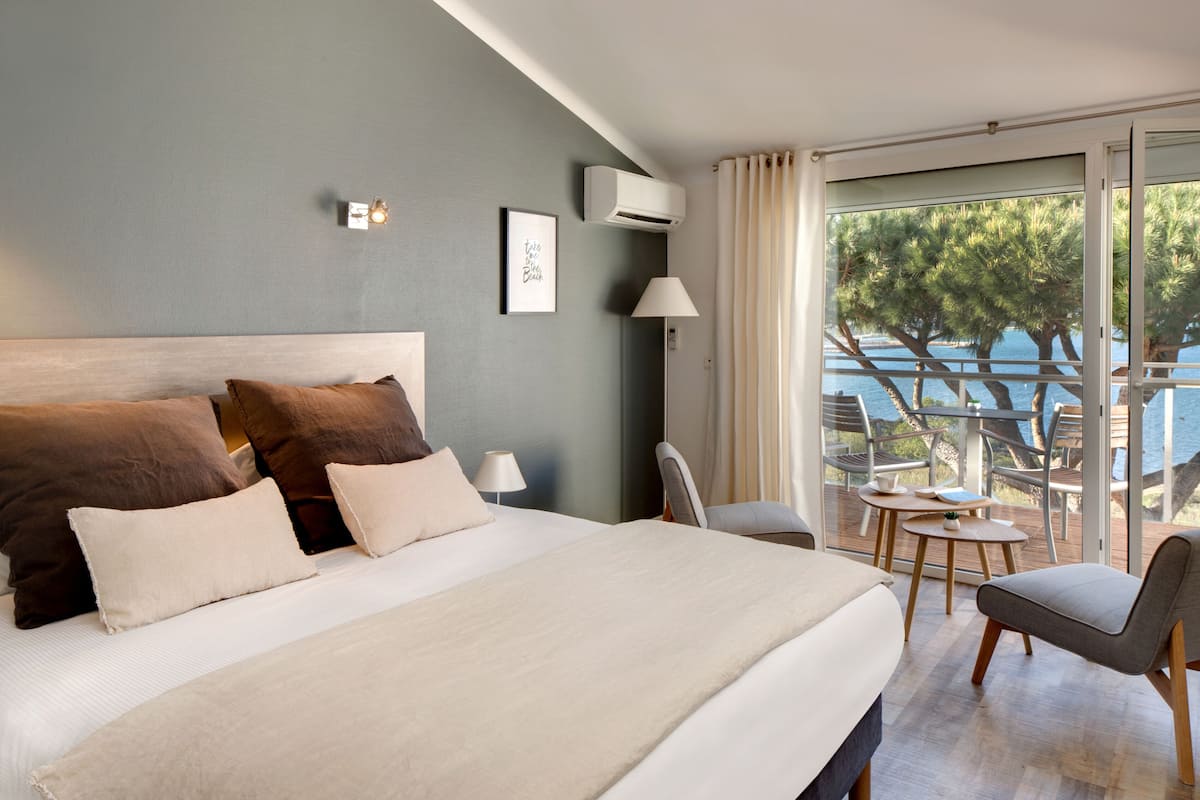 A hotel room with a large bed, a desk, and a balcony with a view of the sea.