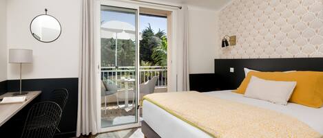 Una habitación de hotel con cama, escritorio, silla, espejo y balcón con mesa y sillas.