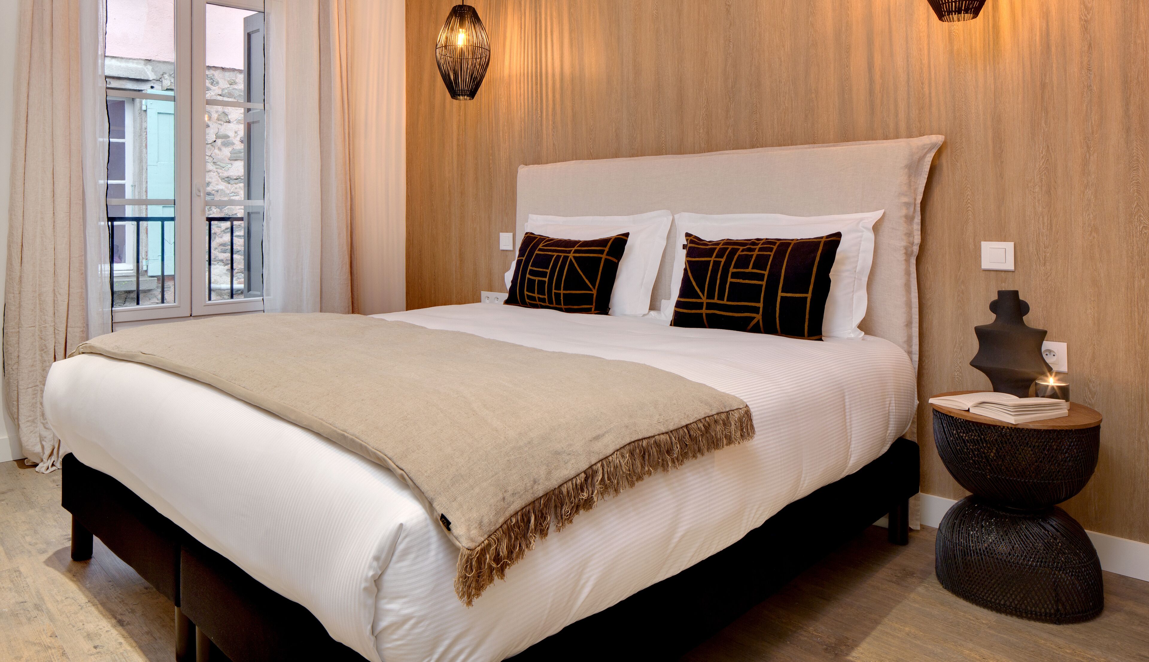 A hotel room with a large bed, a bedside table with a lamp, and a view of the outside balcony.