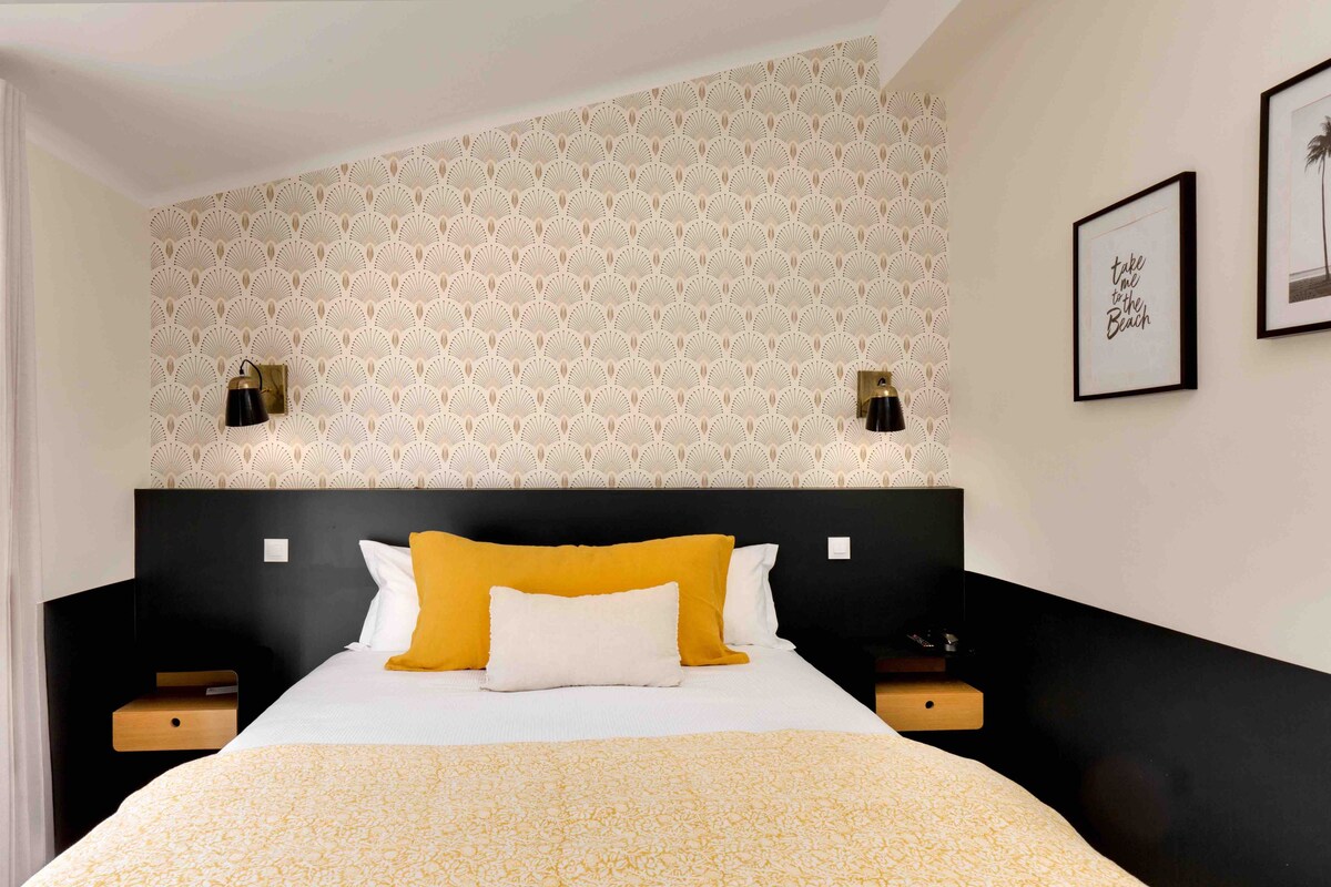 Habitación de hotel con una cama, dos mesitas de noche, un cabecero y una pared con papel tapiz estampado.