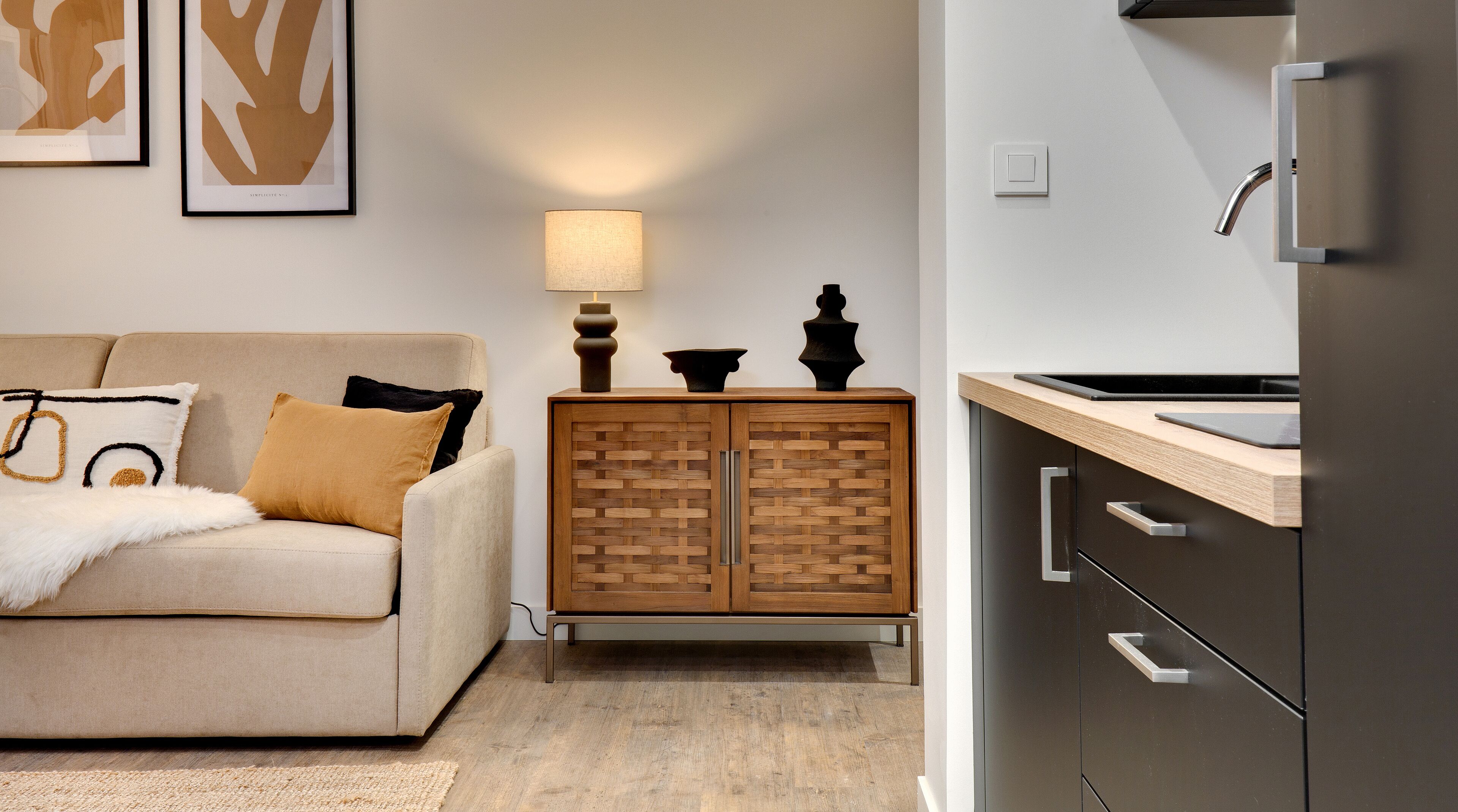 Una sala moderna con un sofá, un aparador de madera y una cocina con refrigerador.