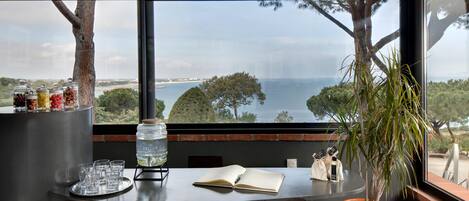 A table with a view of the sea, a potted plant, and a book.