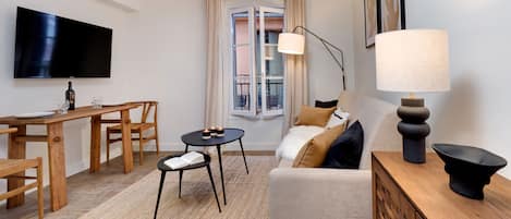 Una sala de estar moderna con una televisión de pantalla plana, muebles de madera, un sofá con cojines, una lámpara de pie y vistas a través de una ventana.
