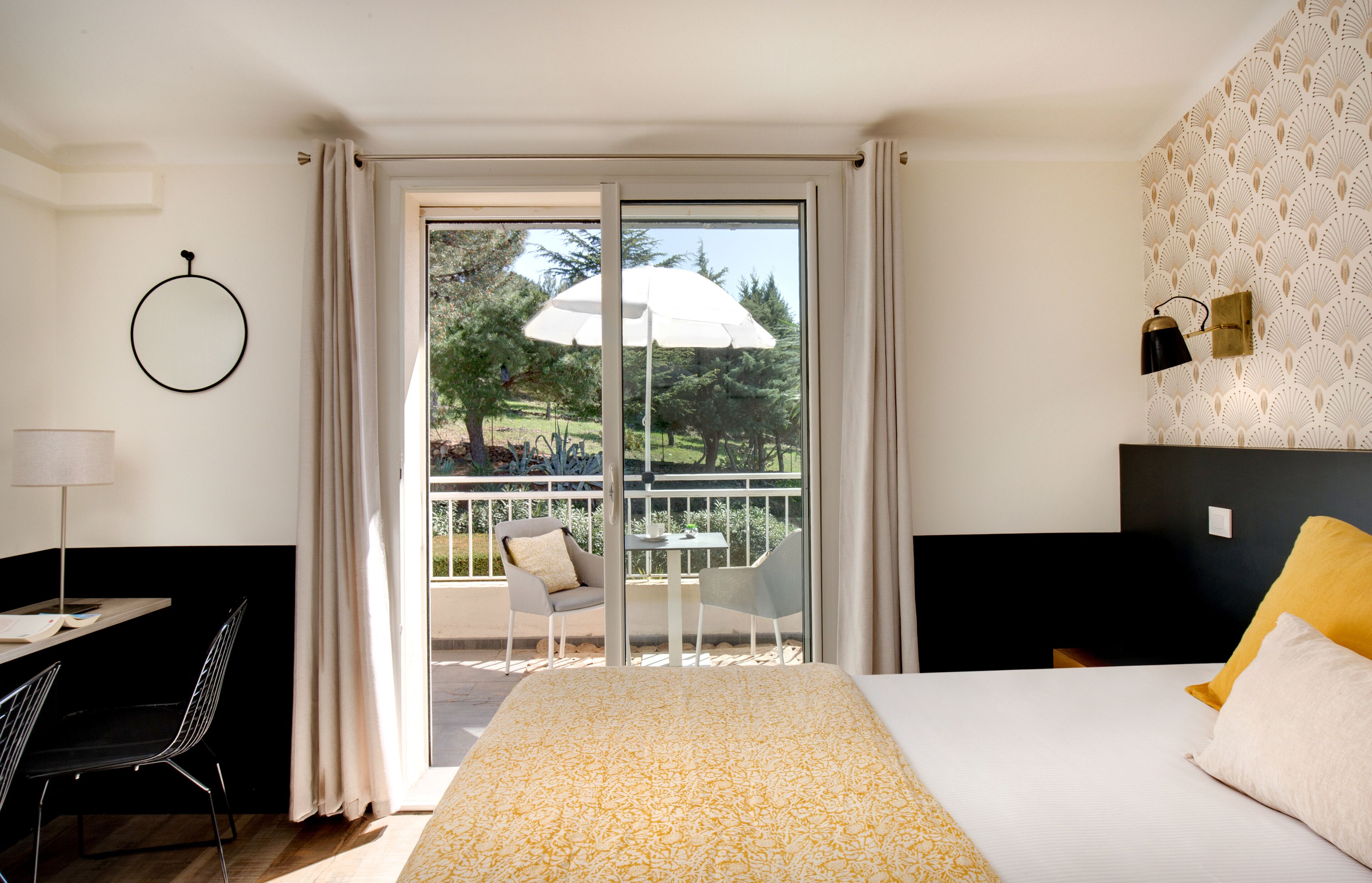 A hotel room with a bed, a desk, a chair, and a balcony with an umbrella.