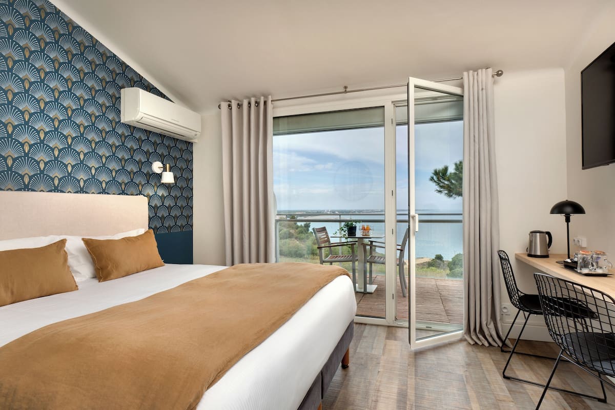 A hotel room with a large bed, a balcony with a table and chairs, and a view of the sea.