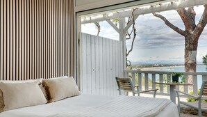 Un dormitorio con cama, almohadas y vista al océano.