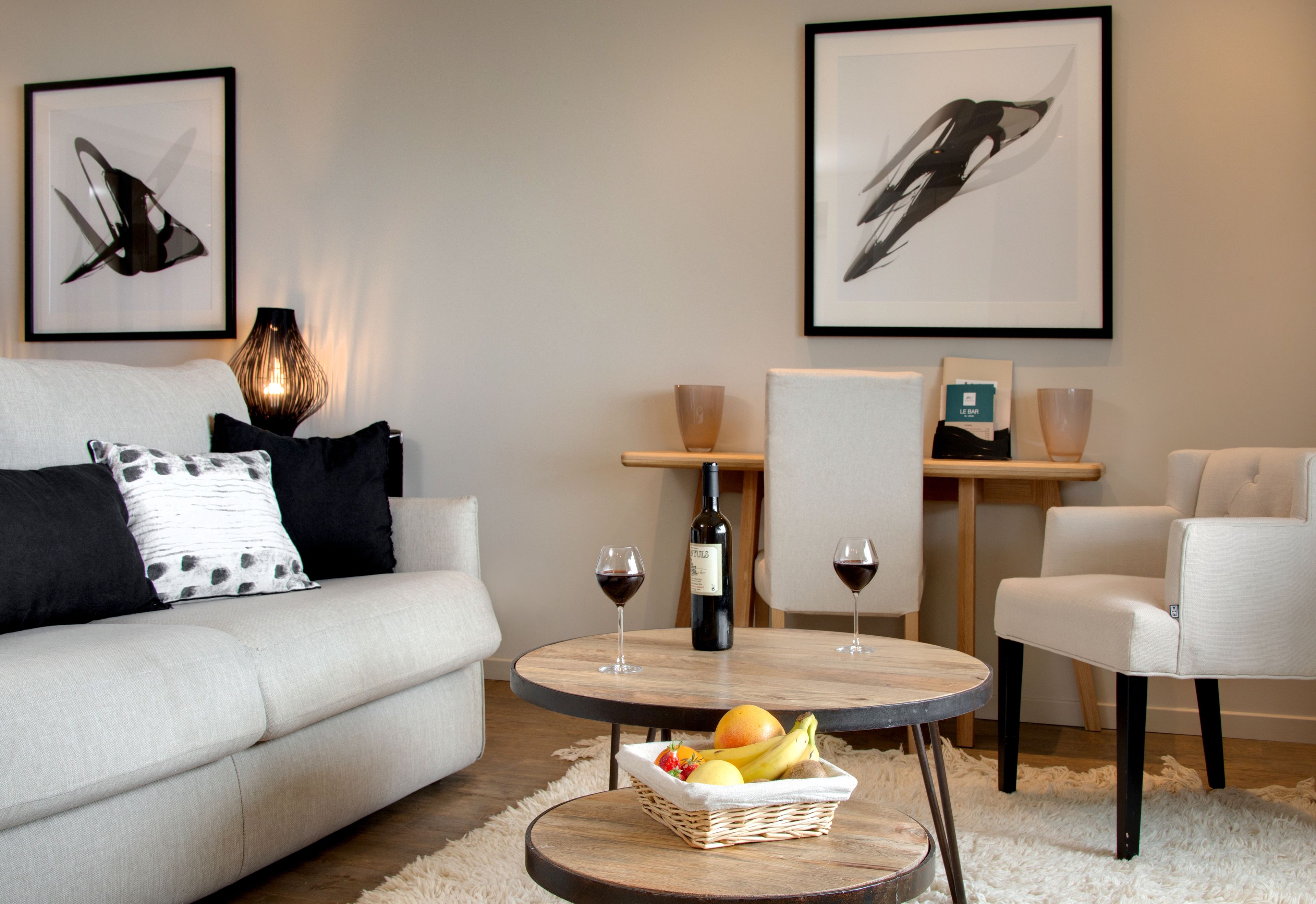 A modern living room with a sofa, a round coffee table with fruits, two wine glasses, and a bottle of wine.