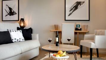 A modern living room with a sofa, a round coffee table with fruits, two wine glasses, and a bottle of wine.