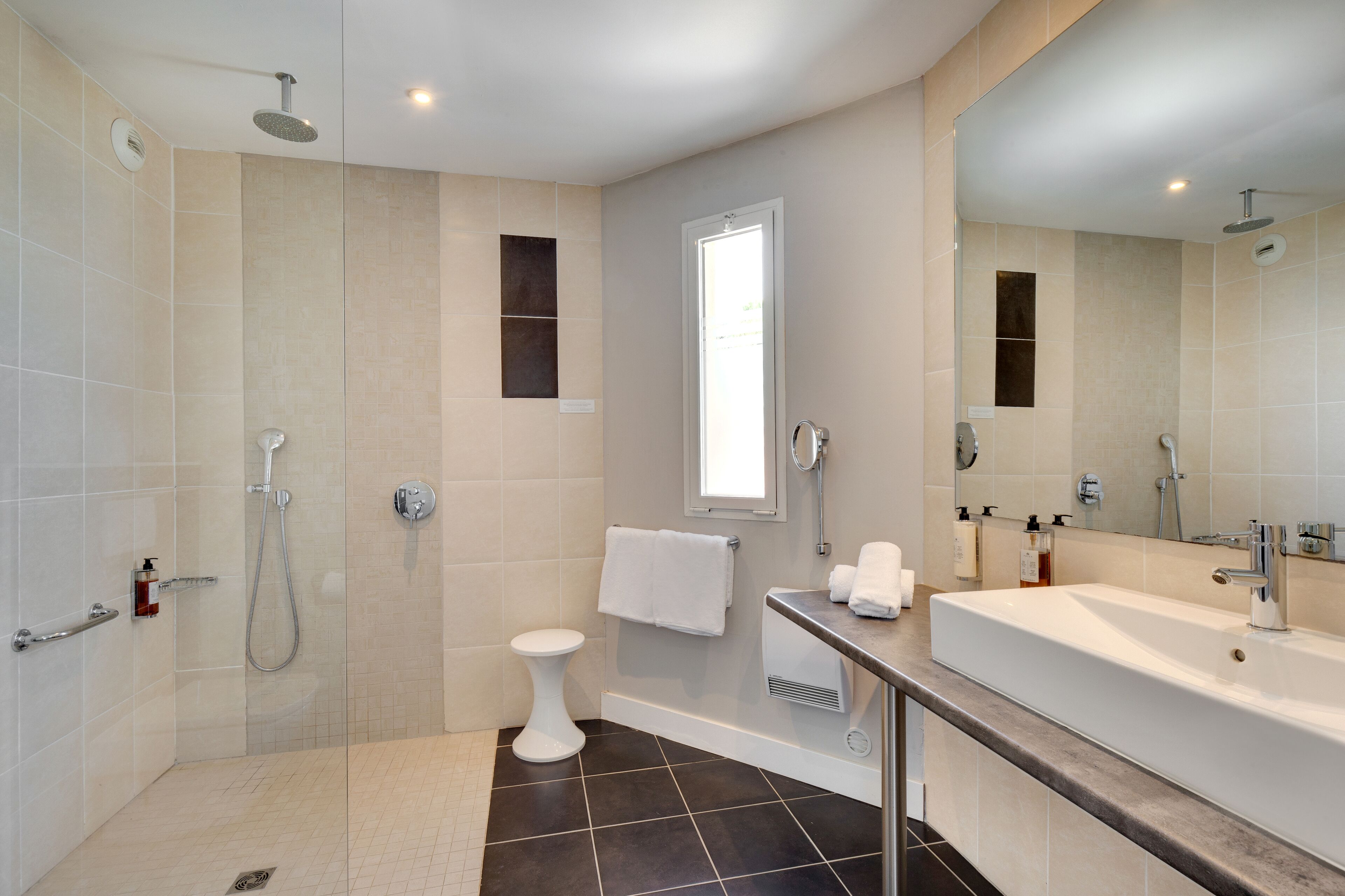 A modern bathroom with a glass-enclosed shower, a white pedestal toilet, a large mirror, and a bathtub.