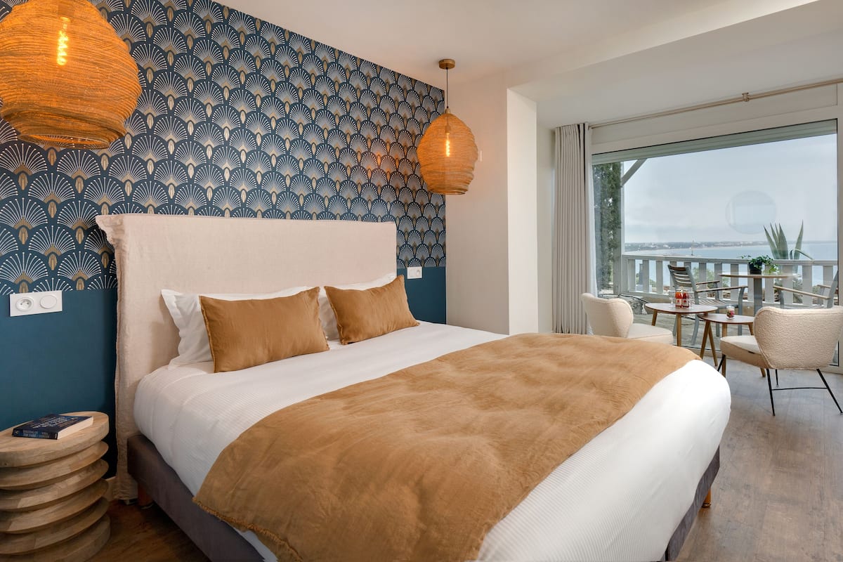 A bedroom with a large bed, a patterned wall, and a balcony with seating.