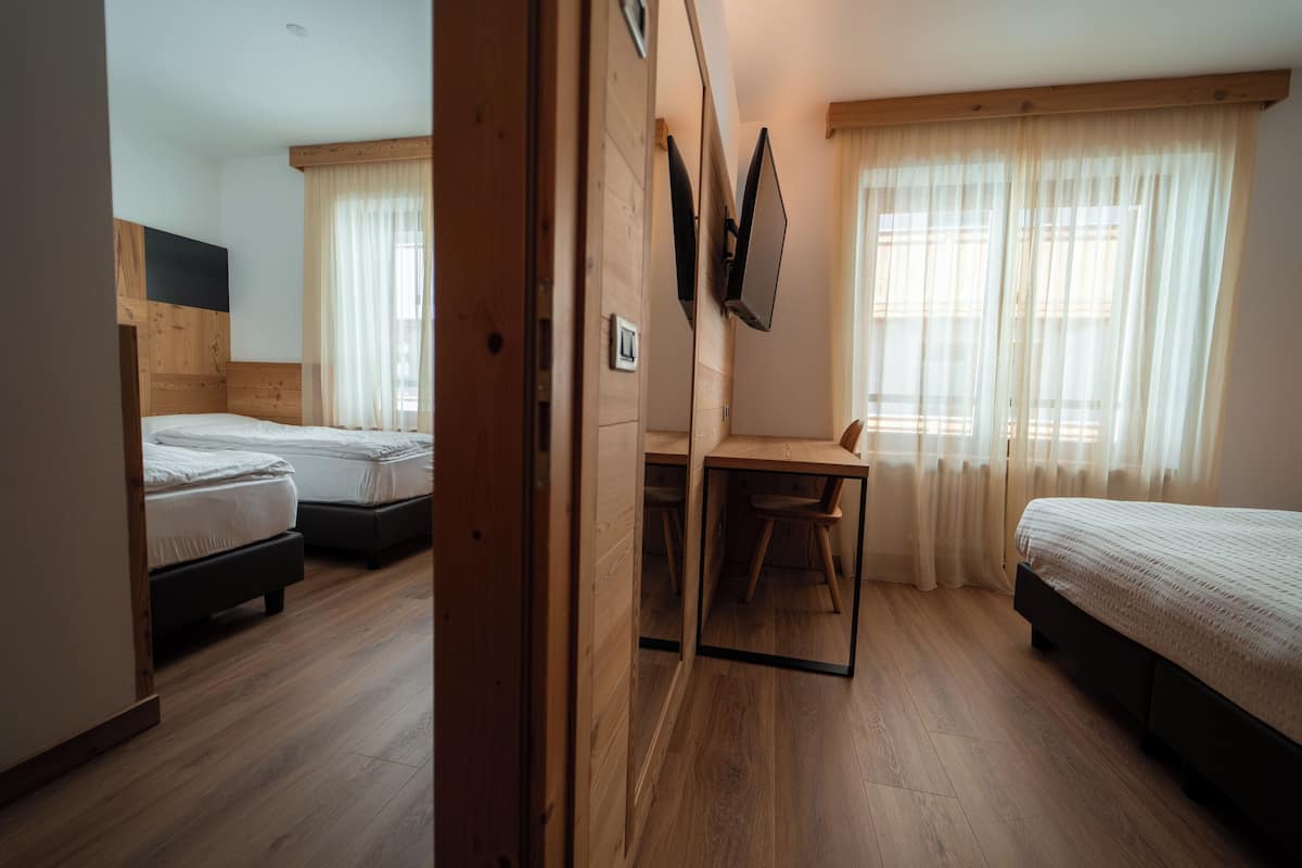Habitación con dos camas, un escritorio y una silla. Se observa un espejo en la pared y una ventana con cortinas.