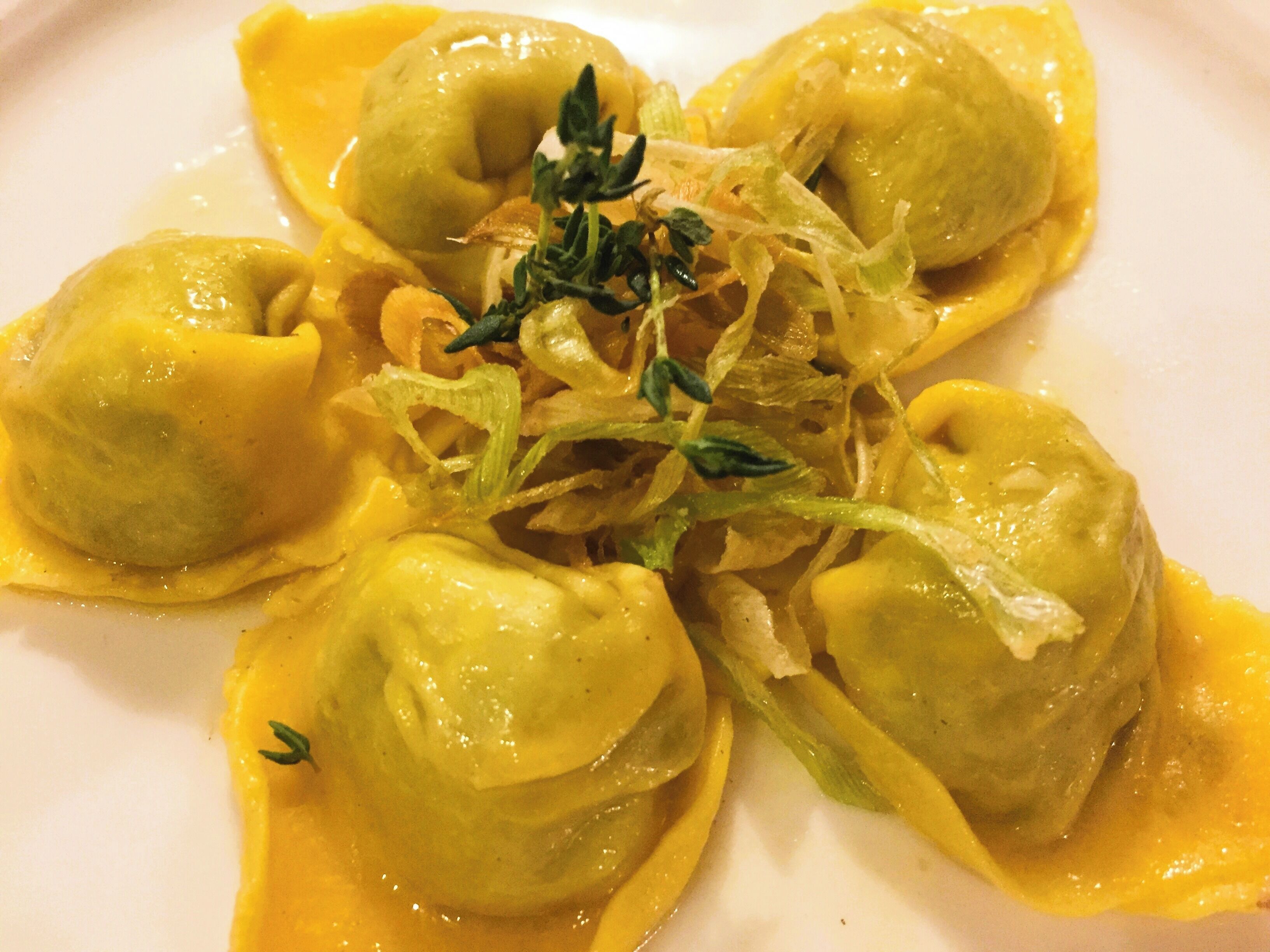 A plate of ravioli with a creamy sauce and garnished with herbs.