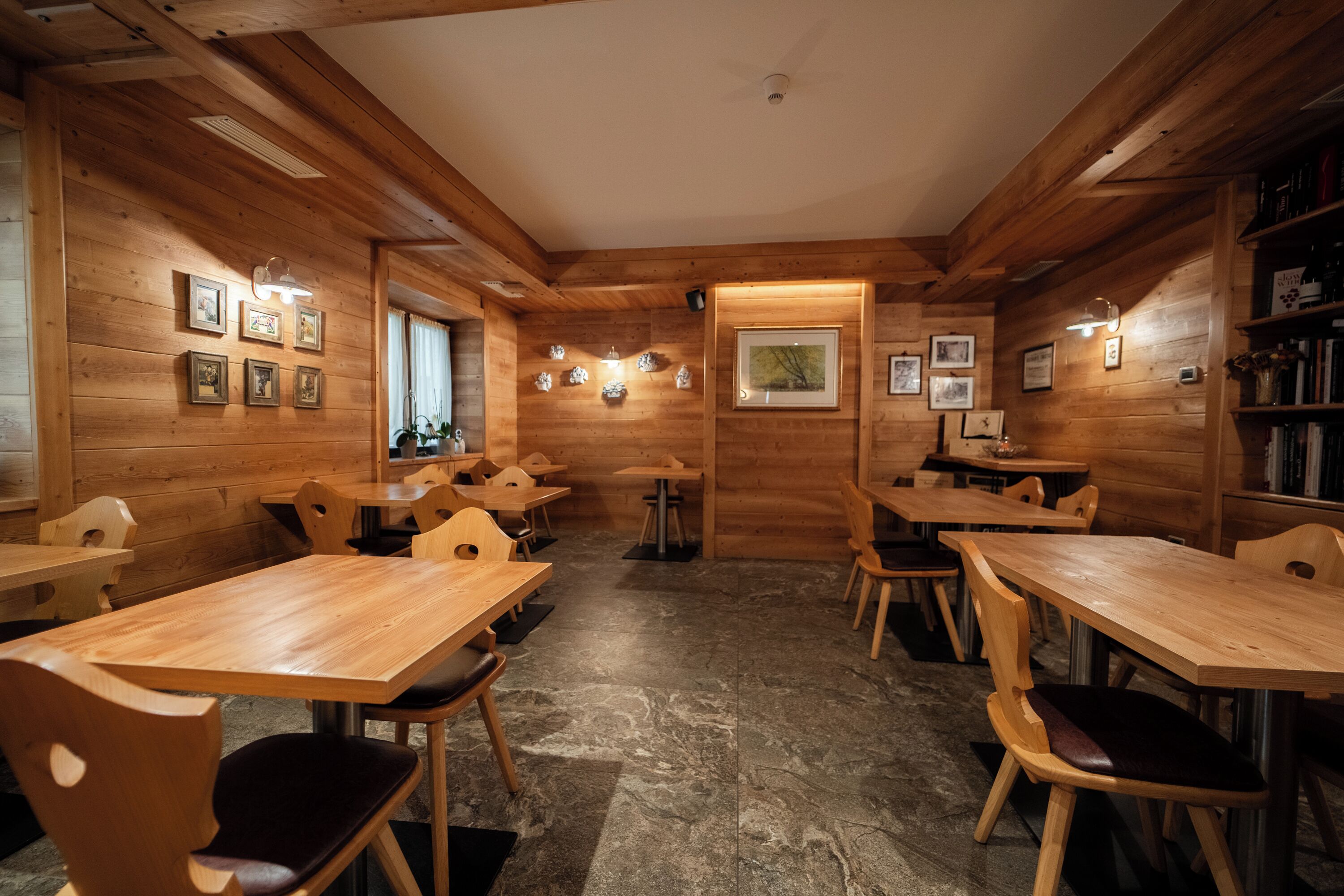 Un interno in legno accogliente, con diversi tavoli e sedie, quadri appesi alle pareti e un pavimento in pietra.