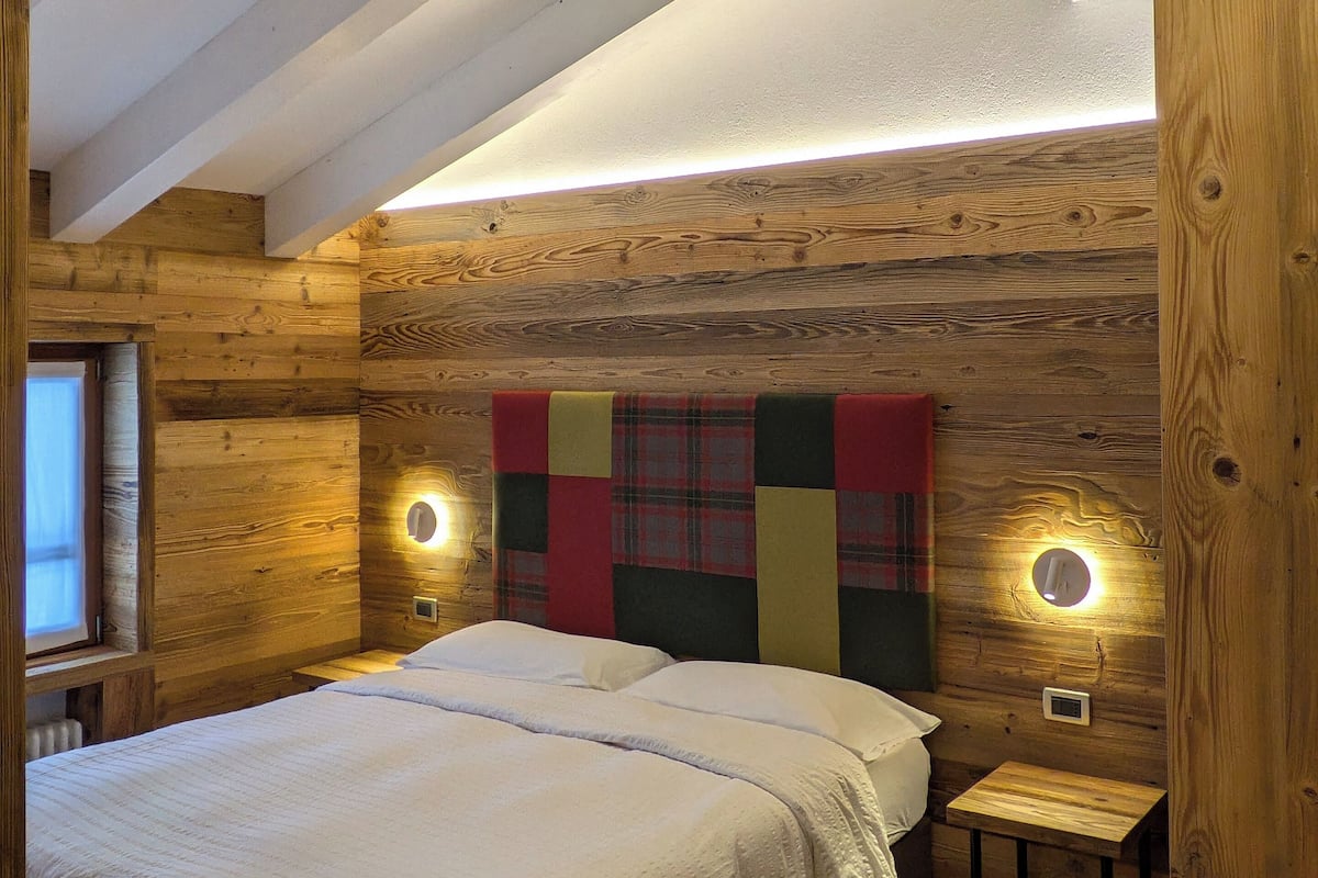 Un dormitorio acogedor con techo de madera, una cama grande, dos mesitas de noche y un edredón colorido en el cabecero.