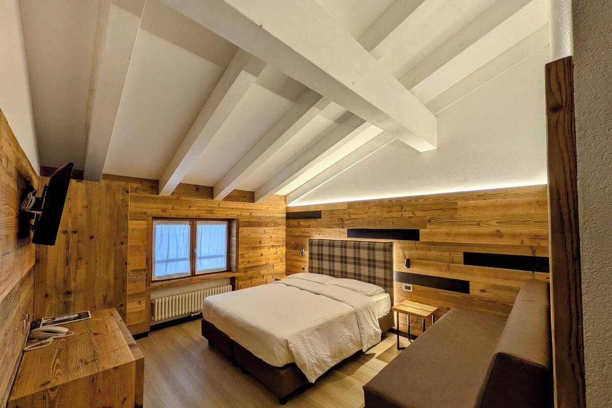 Un dormitorio con techo inclinado, paredes de madera, una cama, una mesita de noche y una ventana, además de un banco empotrado.
