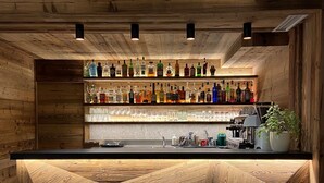 A bar with a wooden counter and shelves of various liquor bottles. - Hotel Ariston (Pinzolo)