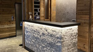 A reception area with a marble counter, wooden panel walls, and a modern design. - Hotel Ariston (Pinzolo)