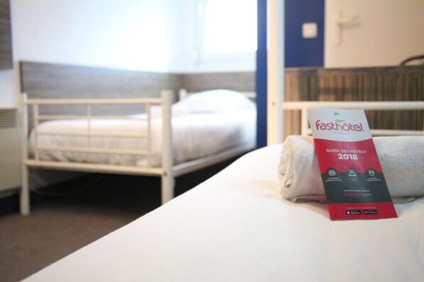 A hotel room with a neatly made bed, a folded guide for 2018, and a visible window.
