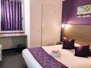 Hotelkamer met een bed, een raam met paarse gordijnen, een hoofdeinde met verlichting en een prullenbak.