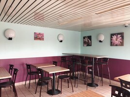 Un interior de restaurante con techo de madera, paredes azul claro y moradas, y varias mesas y sillas.