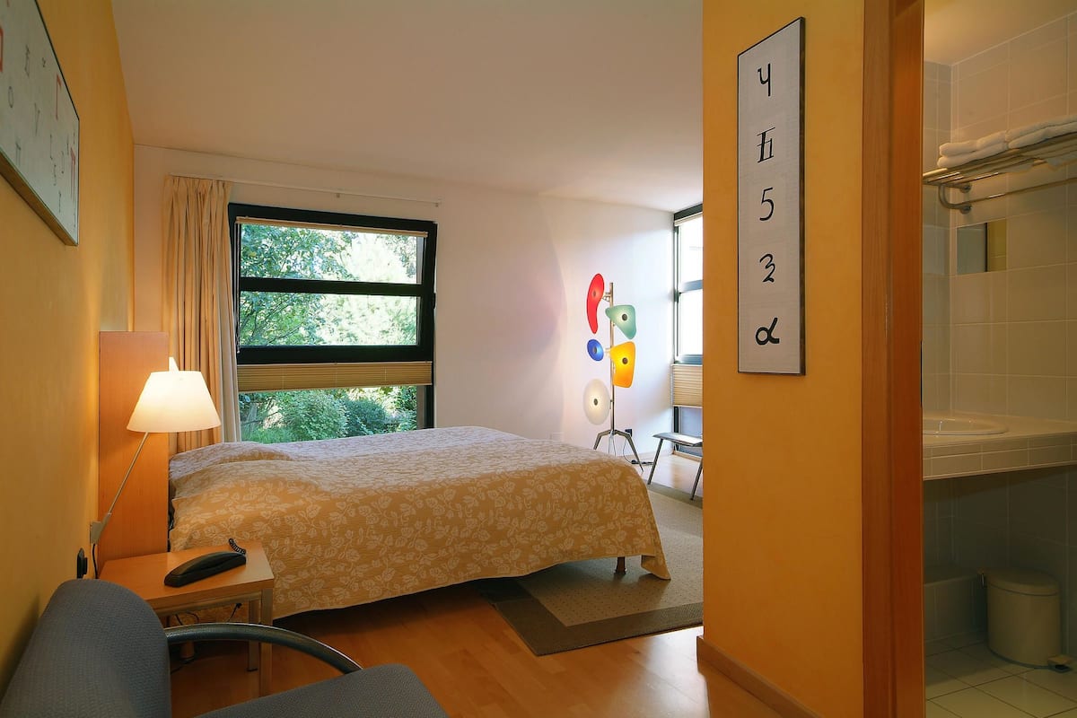 A hotel room with a bed, bedside table, lamp, and a window with curtains.