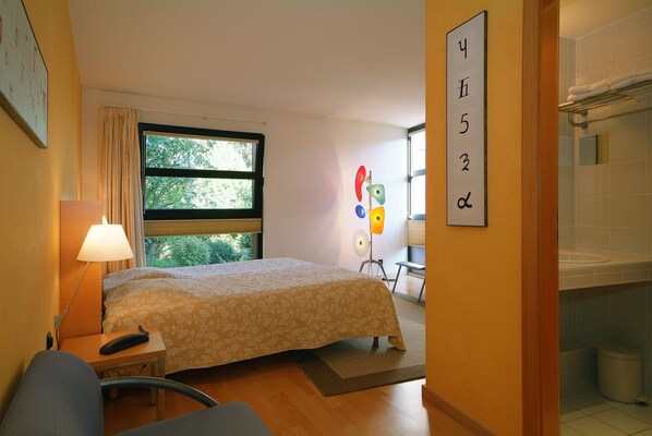 A hotel room with a bed, bedside table, lamp, and a window with curtains. - La Bonneterie (Andlau)
