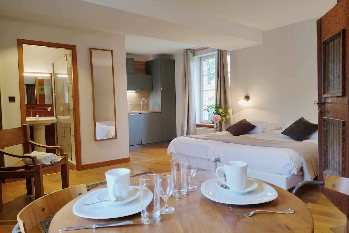 A hotel room with a bed, a dining table with plates and glasses, a mirror, and a kitchenette.