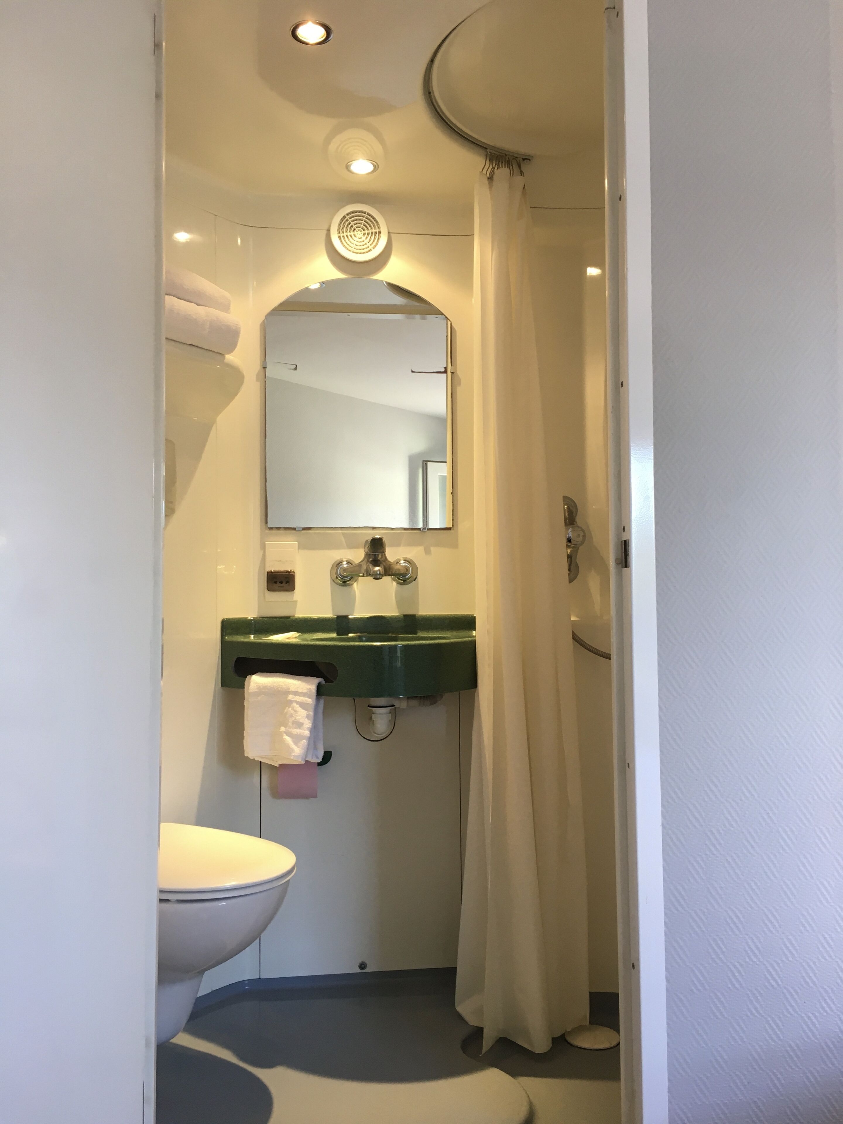 Ein Badezimmer mit einer weißen Toilette, einem grünen Waschbecken, einem Spiegel und einer Duschvorhang.