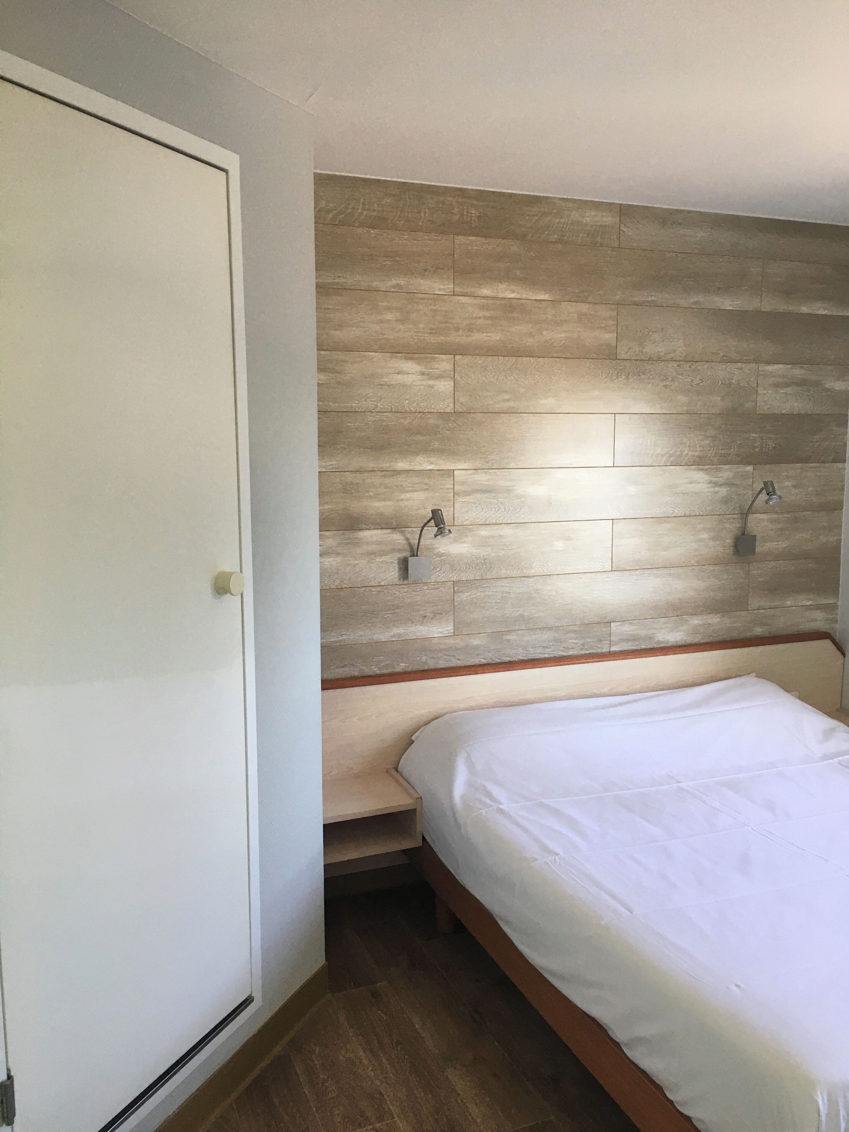 Une chambre à coucher avec une tête de lit en bois, un lit blanc et un petit banc en bois.