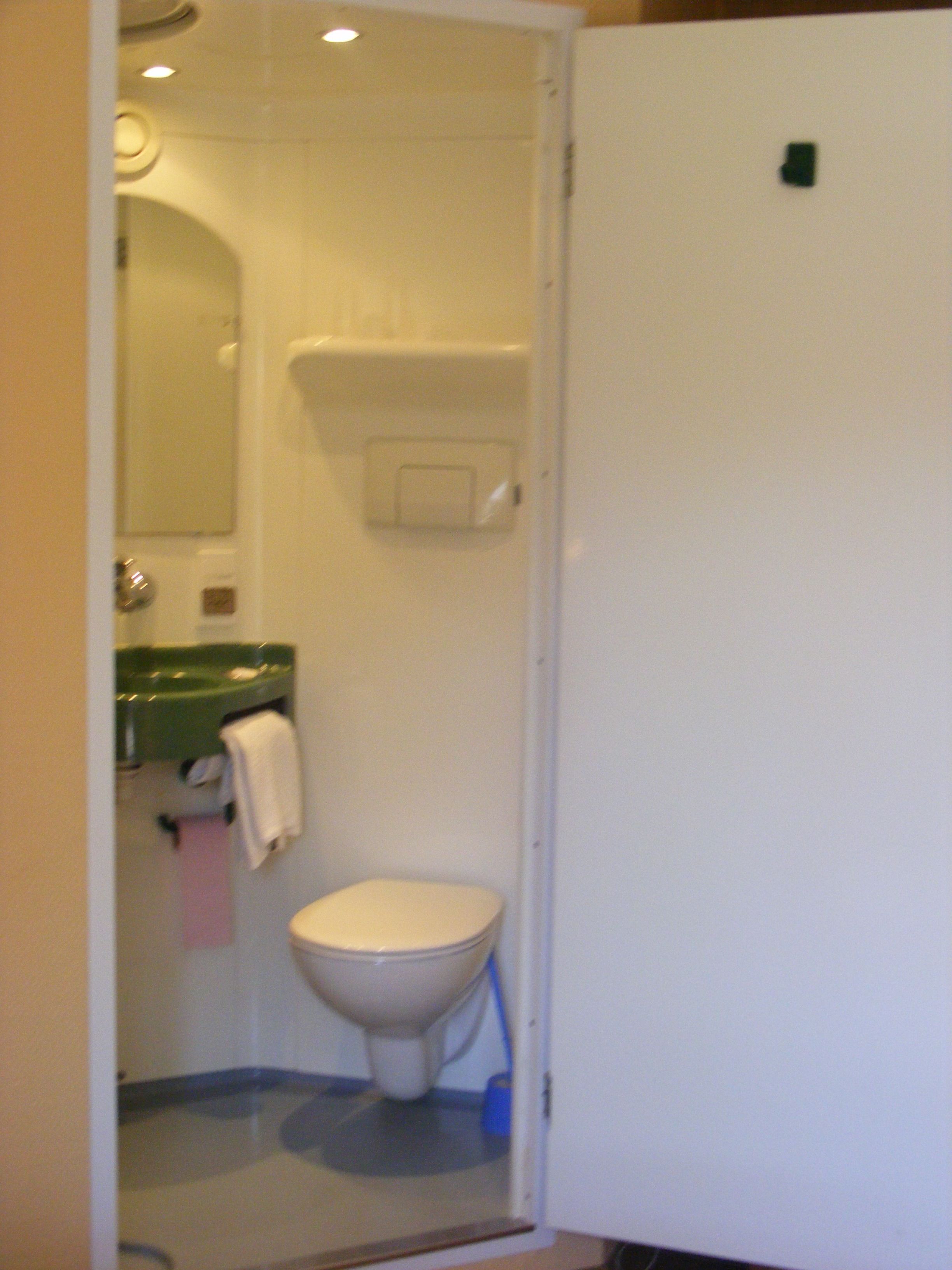 Un baño pequeño con inodoro, un lavamanos verde y un espejo.