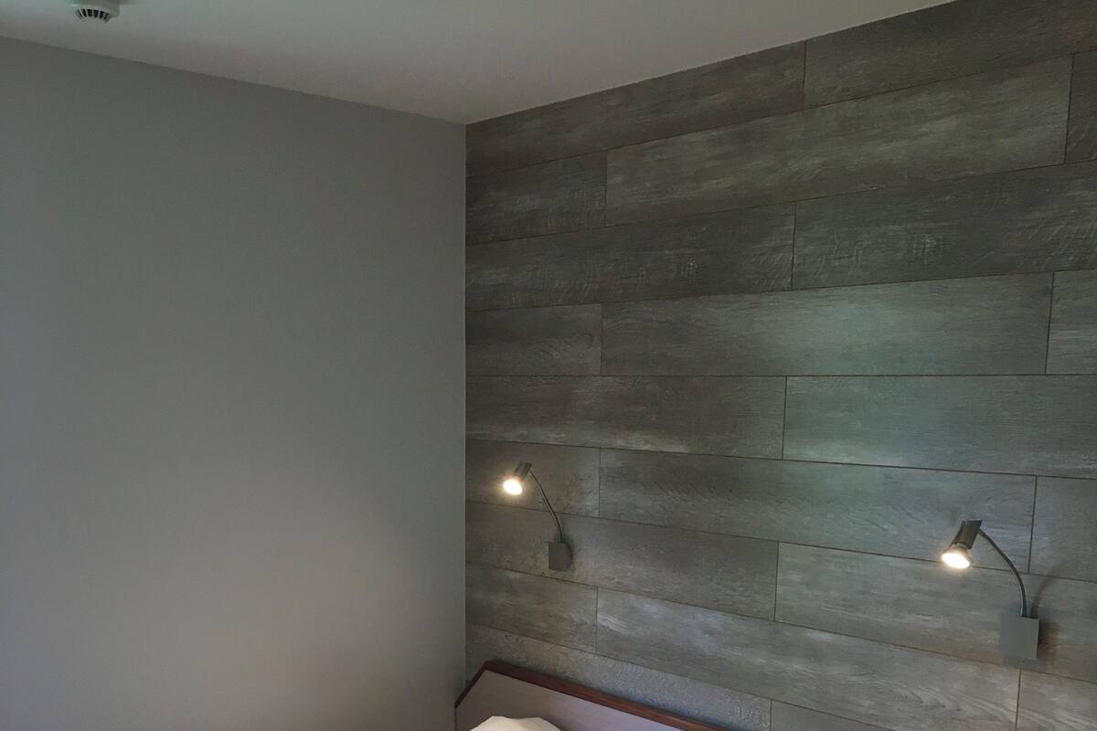 A bedroom with a bed, two bedside lamps, a wooden headboard, and a plain wall.