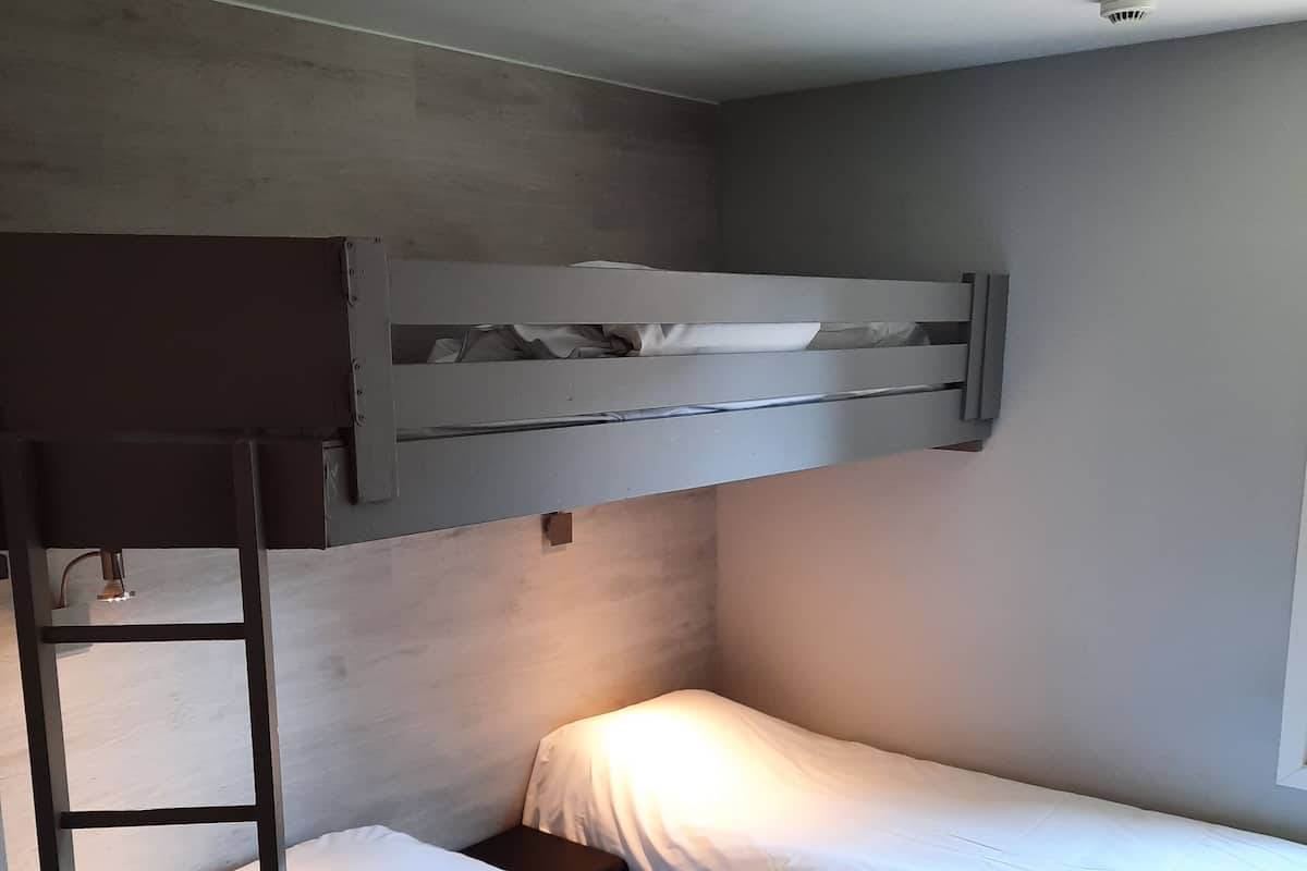 A bunk bed with a ladder, a small bedside table, and a headboard.