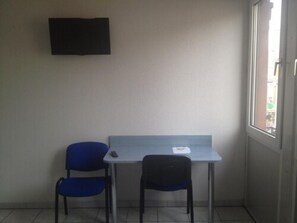 A small room with a single table and two chairs, a flat-screen TV mounted on the wall, and a window providing a view of the outside.