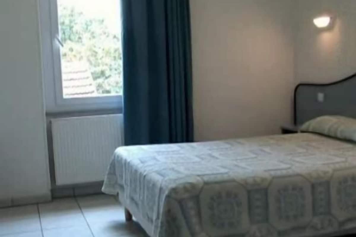 A bedroom with a bed, a window with curtains, and a radiator.