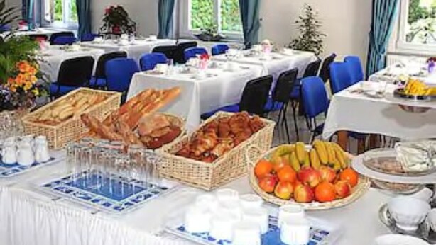 Comedor con mesas dispuestas para el desayuno, con pan, frutas y bebidas.