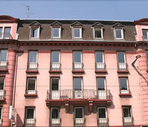 A multi-story building with a pink facade, multiple windows, and balconies with metal railings.