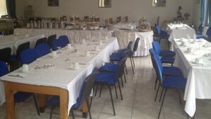 Un salón de banquetes con varias mesas redondas dispuestas para comer, sillas azules y manteles blancos.