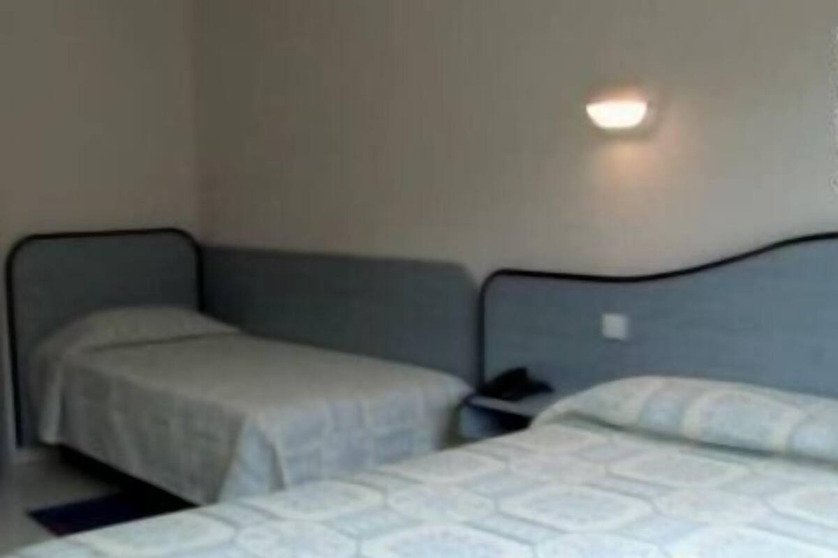 A small, single-room hotel room with two single beds, a nightstand, and a wall-mounted light.