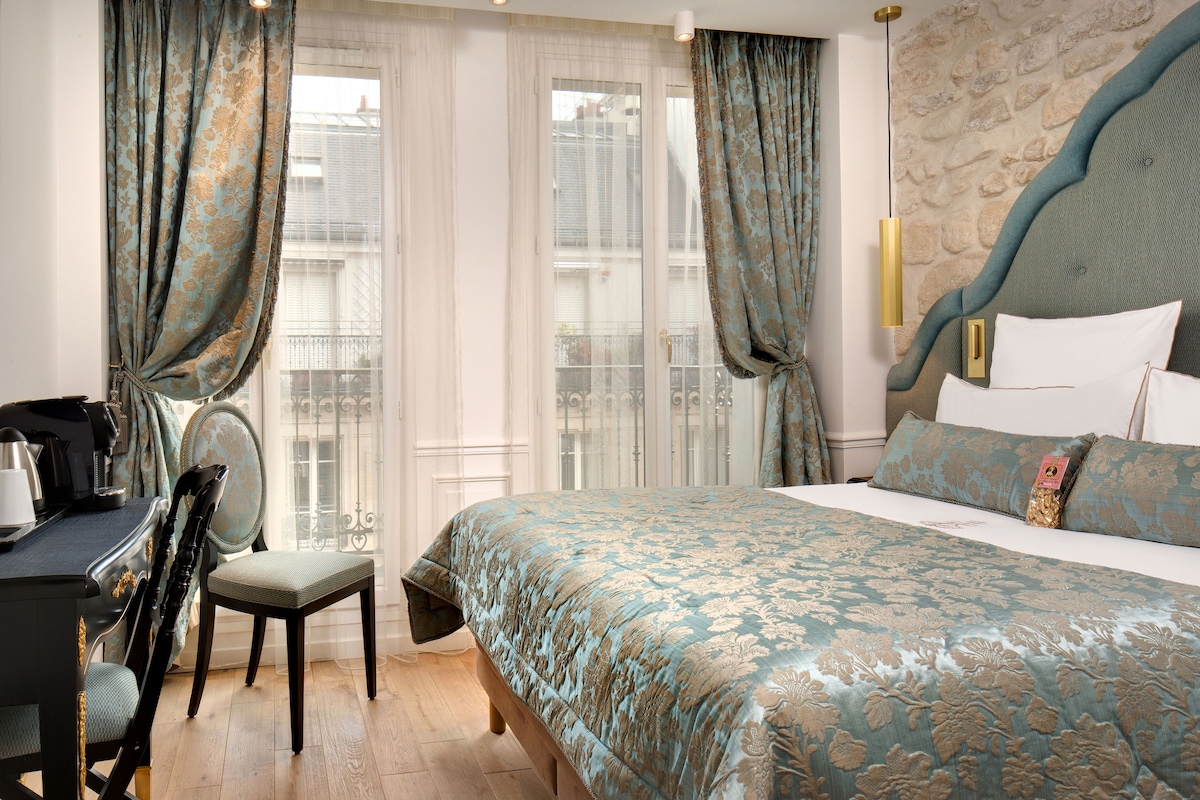 Habitación de hotel con una cama grande, un escritorio con silla y vistas al exterior a través de una ventana con cortinas.