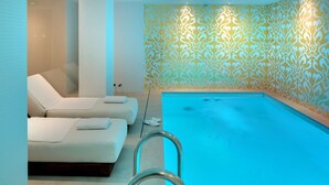 A modern indoor pool area with a clear blue pool, two white lounge chairs, and a patterned wall. - Hôtel Kleber Paris & Spa (Paris)