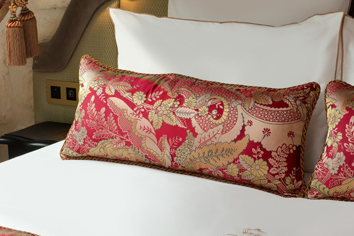 A bed with a white and red patterned bedspread, a white pillow, and a red and gold pillow.