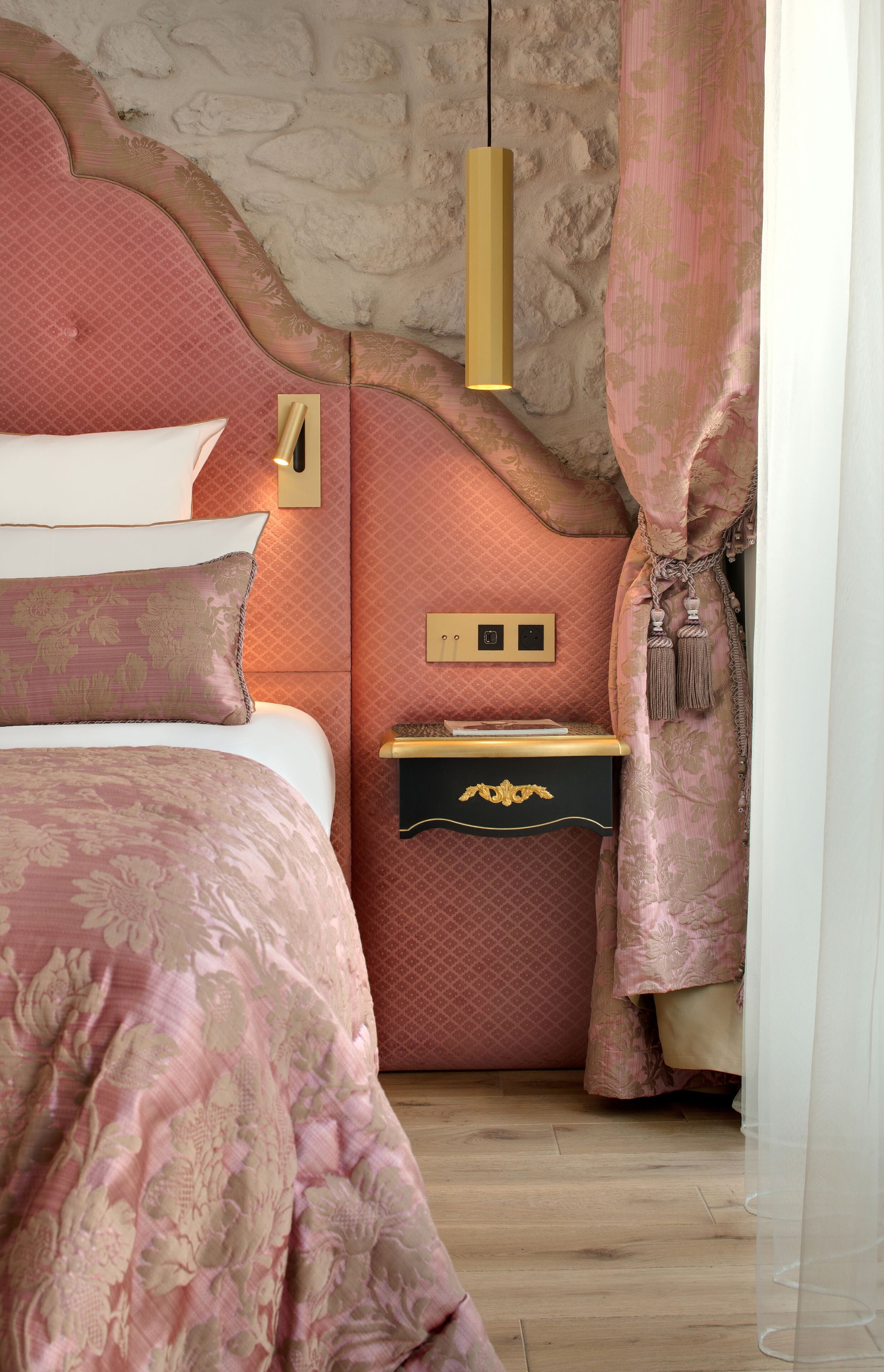A bedroom with a large bed, a nightstand with a lamp, and a wall-mounted light fixture.